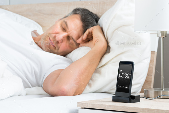 Man On Bed With Alarm On A Cell Phone Display