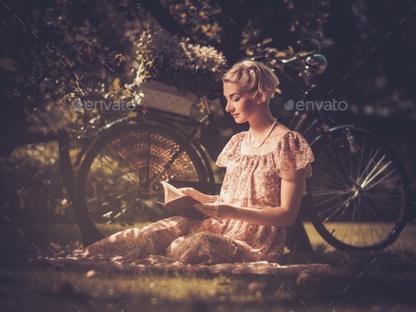 Blond retro woman with a book in summer dress sitting on a meadow (Misc) Photo Download