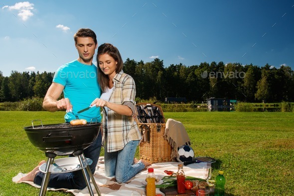 Young couple preparing sausages on a grill outdoors (Misc) Photo Download