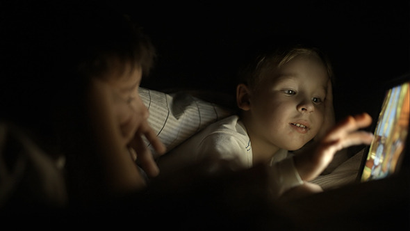 Two Boys Lying In Bed At Night And Using Pad Two Boys Lying In Bed At Night And Using Pad