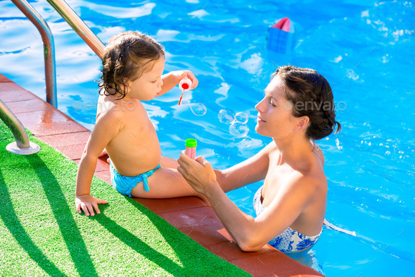 Baby girl blowing soap ballons with mother in pool