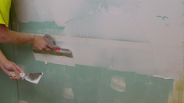 Construction Worker Applying Plaster on a Drywall Construction Worker Applying Plaster on a Drywall