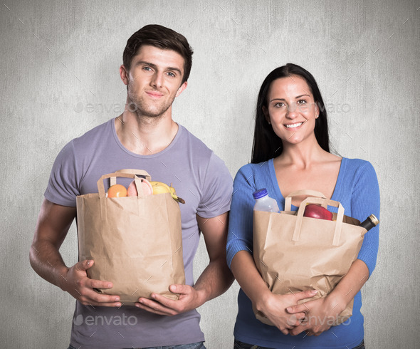 Young couple holding grocery bags against weathered surface (Misc) Photo Download