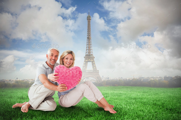 Happy couple sitting and holding heart pillow against eiffel tower (Misc) Photo Download