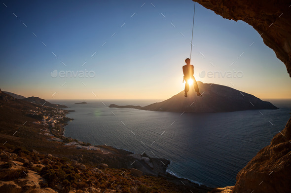 Rock climber hanging on rope while lead climbing at sunset. (Misc) Photo Download