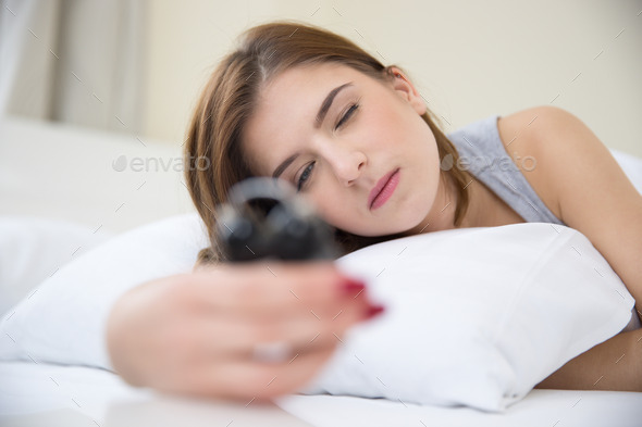 Sleepy woman looking at alarm clock alarm in the bed