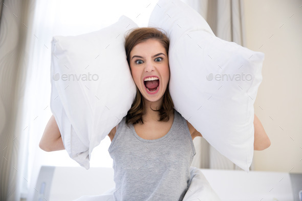 Angry young woman covering her ears with pillows