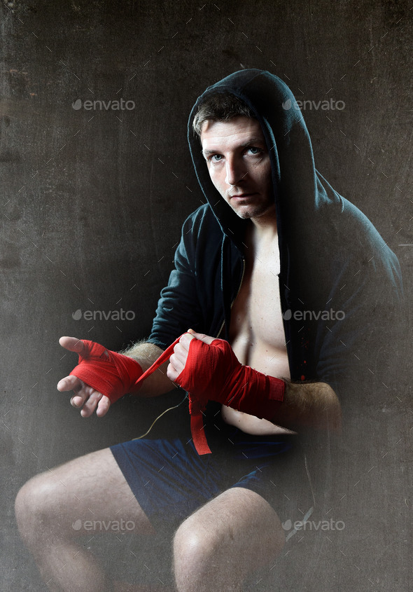 man in boxing hoodie jumper with hood on head wrapping hands wrists before gym training
