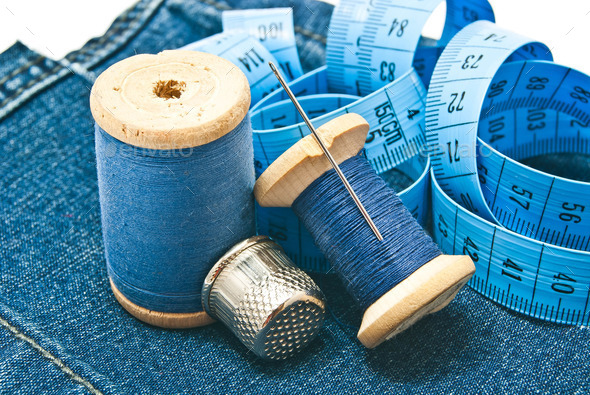 thimble, meter and spools of thread on denim