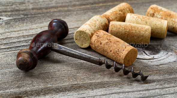 Old corkscrew with used corks in background on aged wood