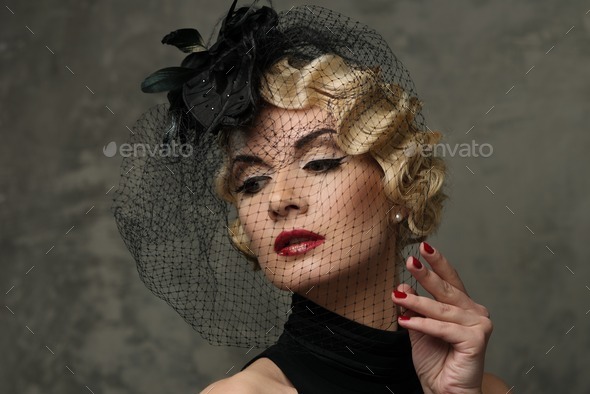 Elegant blond retro woman with red lipstick wearing little hat with veil