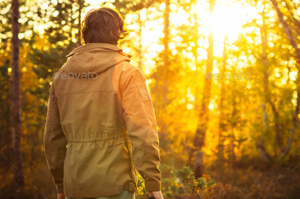 Young Man standing alone in forest outdoor with sunset nature on background
