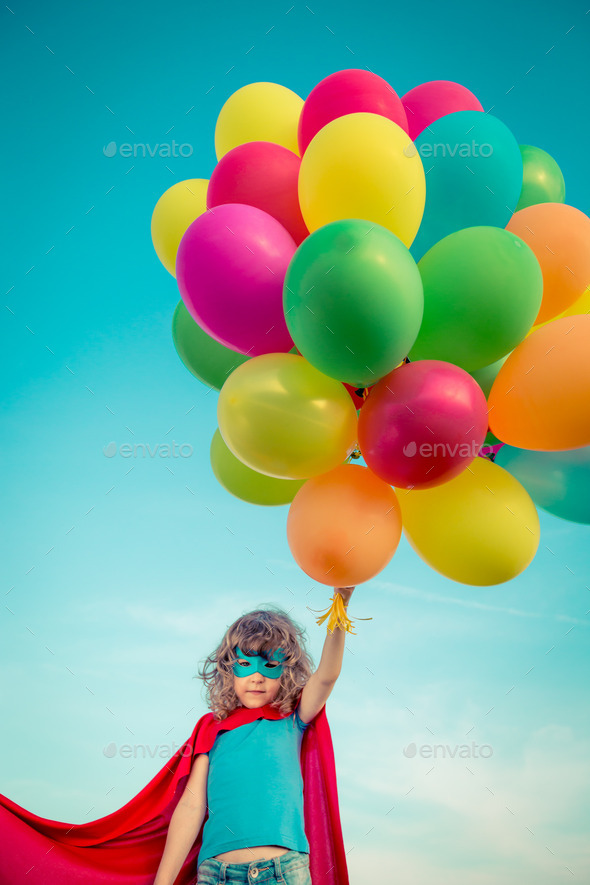 Superhero with toy balloons in spring field