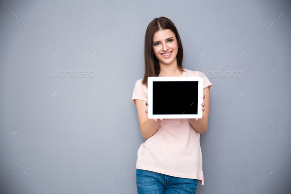 Smiling young woman showing tablet computer screen over gray background