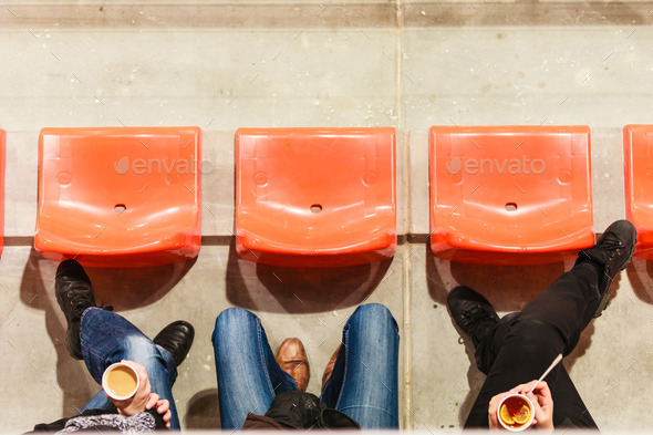 Row of plastic chairs and legs in football stadium.