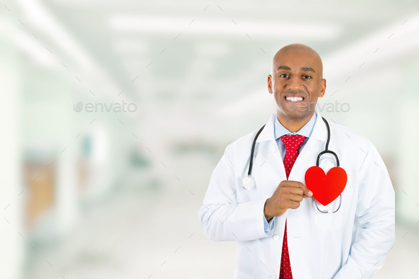Happy doctor holding red heart standing in hospital hallway