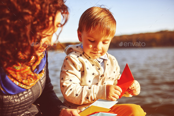Mom and son playing with paper boats by the lake