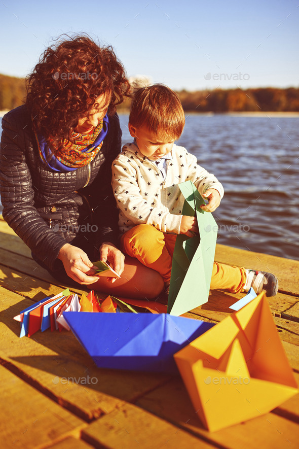 Mom and son playing with paper boats by the lake