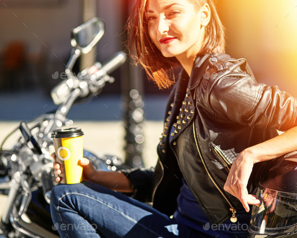 Biker girl in a leather jacket on a motorcycle drinking coffee