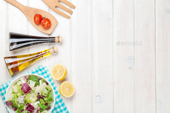 Fresh healthy salad and condiments over white wooden table