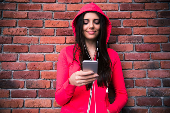 Happy woman using smartphone over brick wall