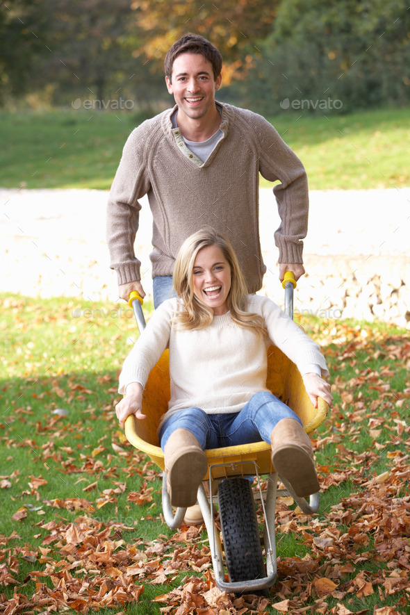 Man pushing wife through autumn leaves on wheelbarrow (Misc) Photo Download