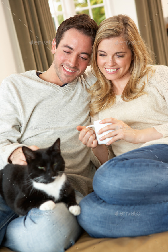 Young couple sitting with cat on sofa with cup in hand (Misc) Photo Download