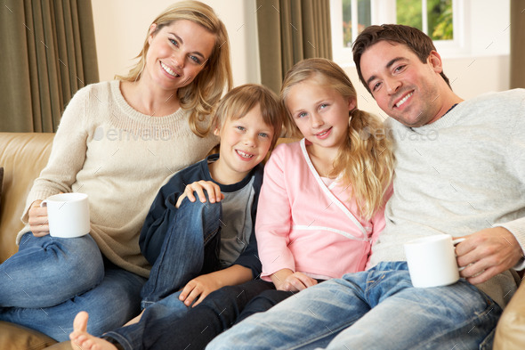 Happy young family sitting on sofa holding cups (Misc) Photo Download