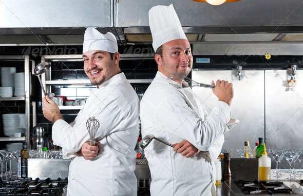 Portrait of two chefs smiling and holding kitchen utensil