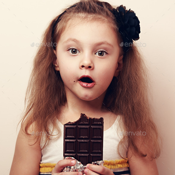 Amazed kid girl looking with open mouth holding chocolate. Close