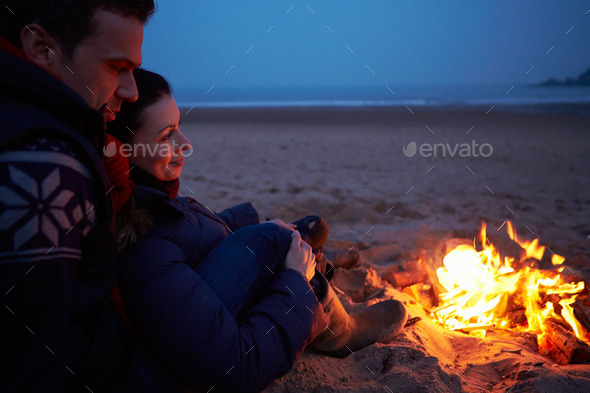 Couple Sitting By Fire On Winter Beach
