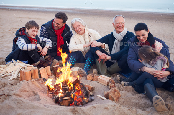 Multi Generation Family Sitting By Fire On Winter Beach