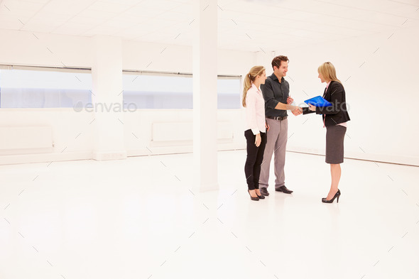 Estate Agent Shaking Hands With Clients In Empty Office