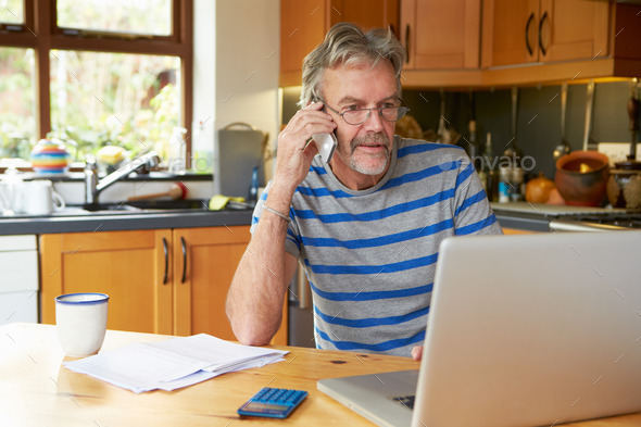 Mature Man Using Mobile Phone Looking At Home Finances