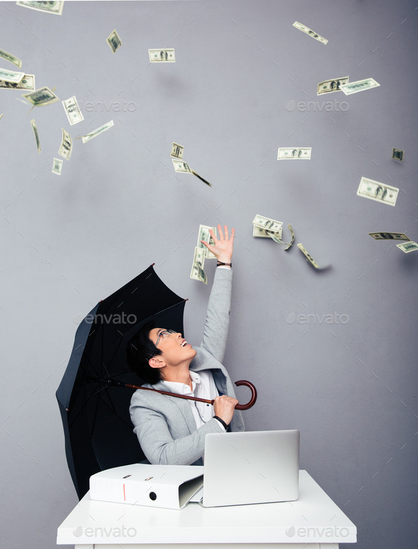 Businessman sitting at the table with rain of money