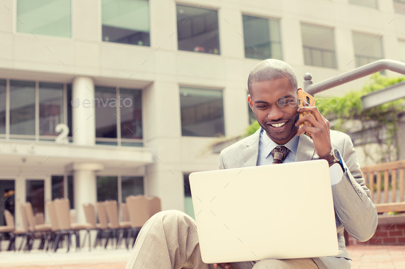 Businessman working with laptop outdoors talking on mobile phone