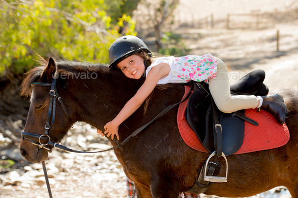 sweet young girl hugging pony horse smiling happy wearing safety jockey helmet in summer holiday