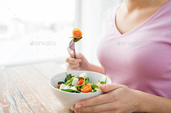 close up of young woman eating salad at home