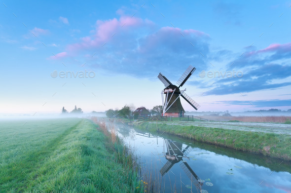 Dutch windmill by river at sunrise
