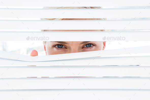 Curious blonde woman looking through venetian blind on a sunny day