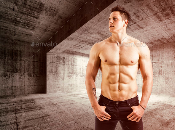 Muscular shirtless young man with jeans, indoors in empty warehouse.