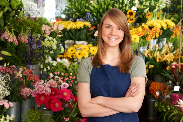 Florist Standing In Shop In Front Of Flower Display