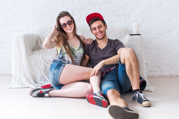 Friends girl and guy sitting on floor at home in summer jeanswear