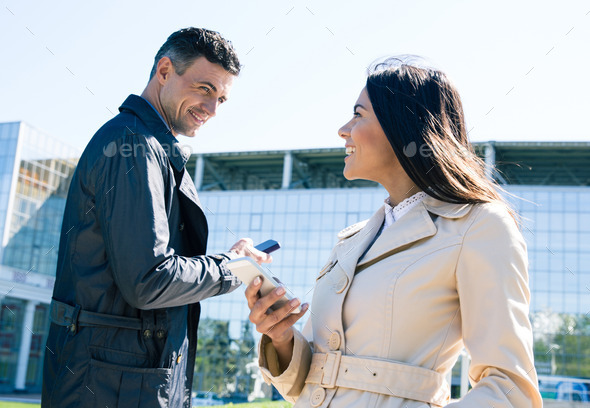 Happy man and woman outdoors with smartphones