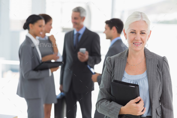 Portrait of confident businesswoman with colleagues behind in office