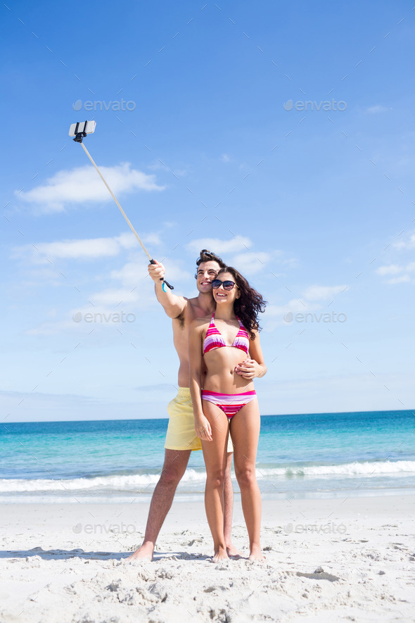 Happy couple taking selfie with selfie stick at the beach (Misc) Photo Download