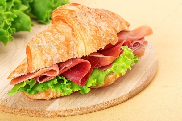 croissant with ham and lettuce on wooden chopping board