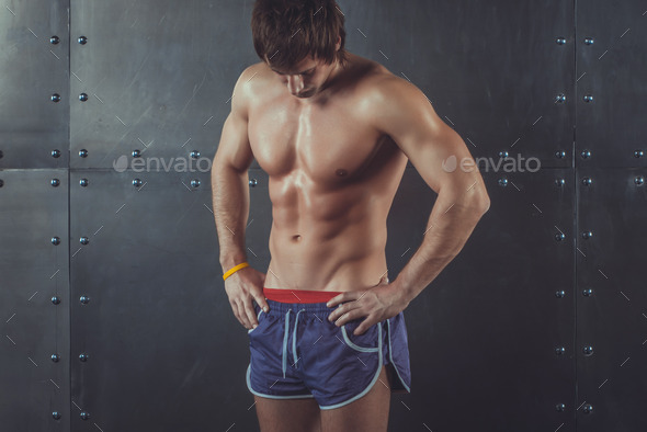 Portrait of fit athletic muscular shirtless young man looking down