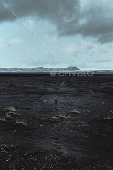 Man walking to a far away mountain on the black sands