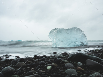 Iceberg being washed away on a black beach.